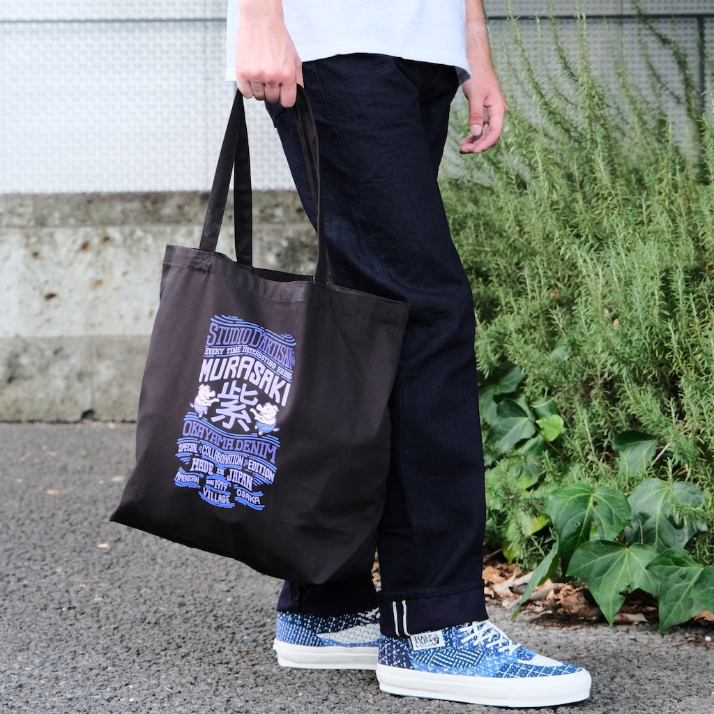 Person holding a black tote bag with custom logo, wearing 15Selvedge denim and blue patterned shoes.