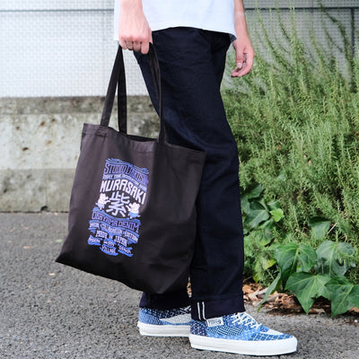 Person holding a black tote bag with custom logo, wearing 15Selvedge denim and blue patterned shoes.